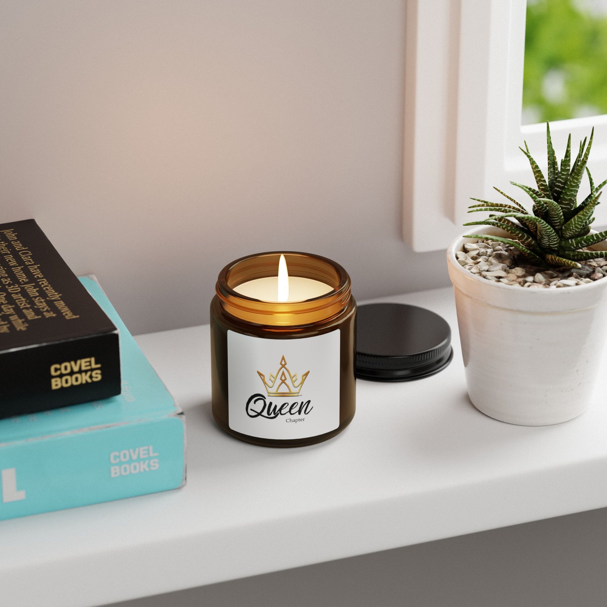 Candle in a jar labeled 'Queen' on a shelf with books and a plant