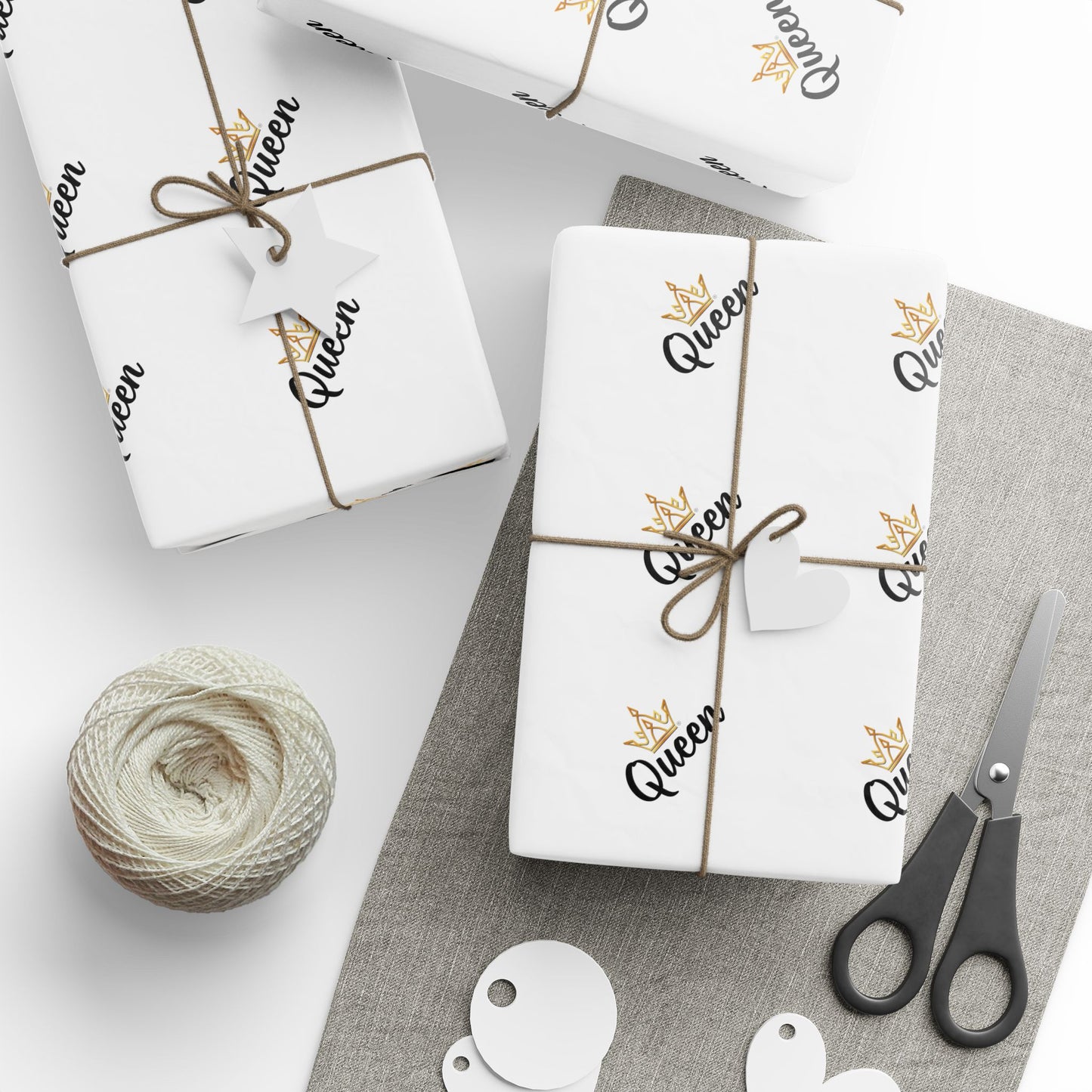 Gift wrap with 'Queen' text and decorative elements on a white surface with scissors and yarn.