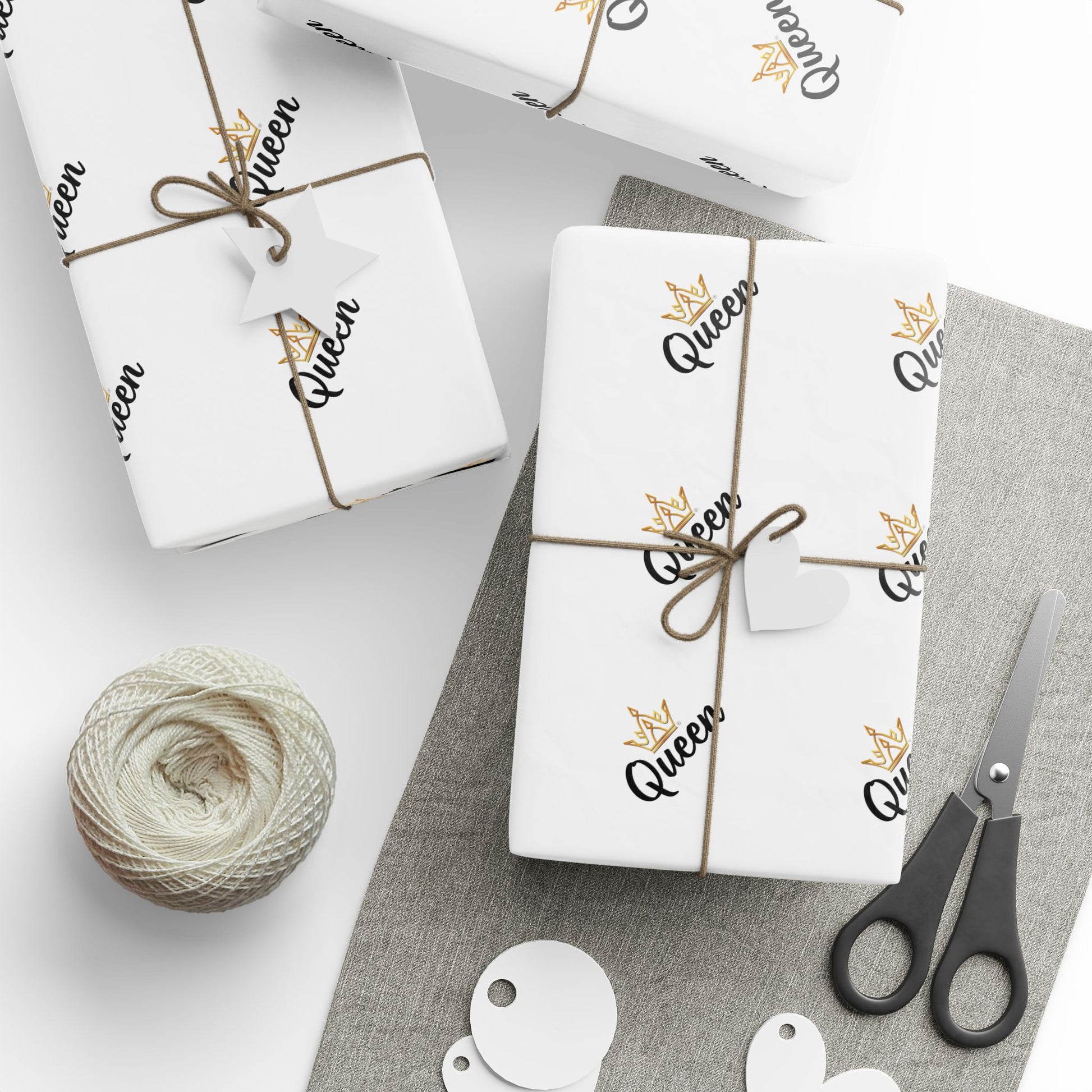 Gift wrap with 'Queen' text and decorative elements on a white surface with scissors and yarn.