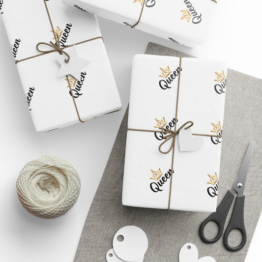 Gift wrap with 'Queen' text and decorative elements on a white surface with scissors and yarn.
