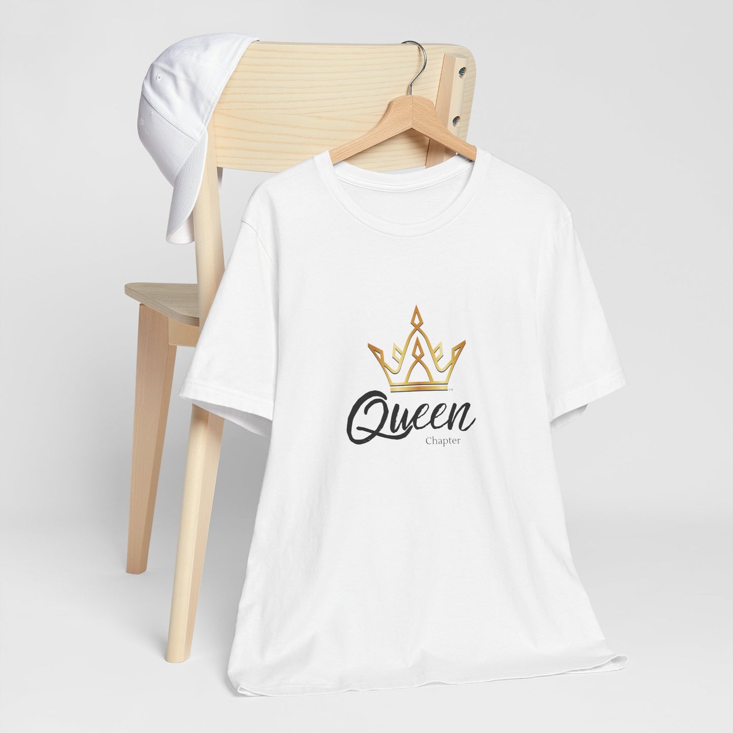 White t-shirt with 'Queen Chapter' design on a wooden chair against a white background